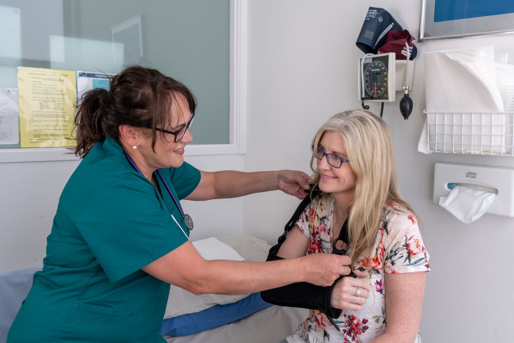 Woman with sling on arm, healthcare worker assisting patient