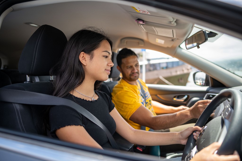 Teenager in driver's seat of car driving with adult in passenger seat