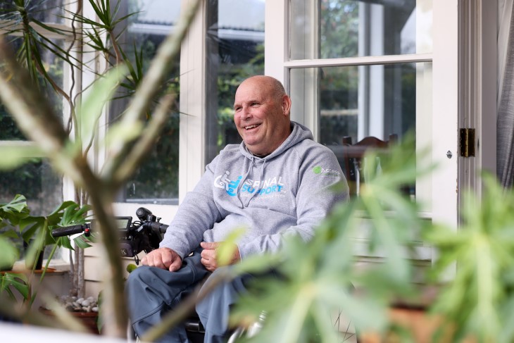 A man in a wheelchair on a porch smiling.