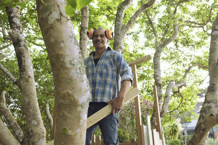 A man putting together a wooden structure in his backyard. 