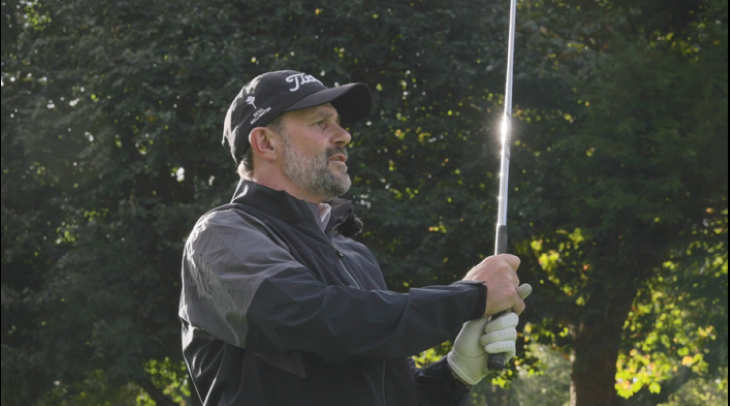 A man holding a golf club after taking a swing