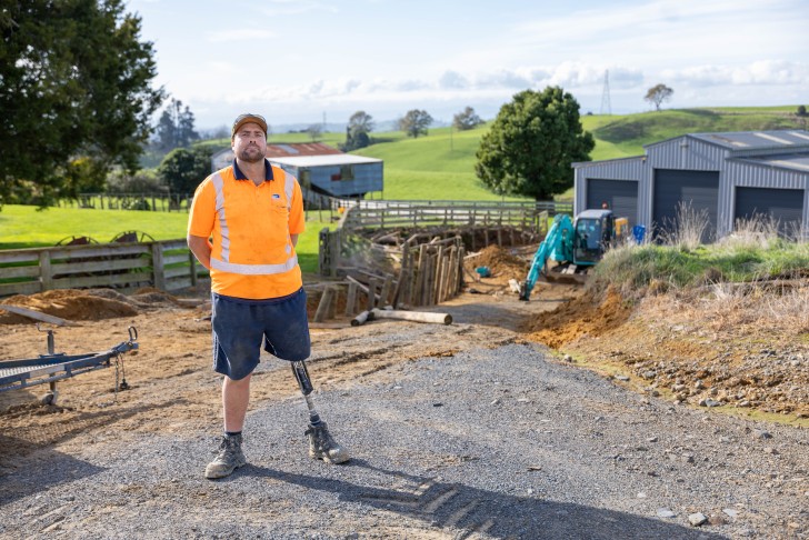 Cory McKinnon wearing his prosthetic leg and standing on a gravel driveway.