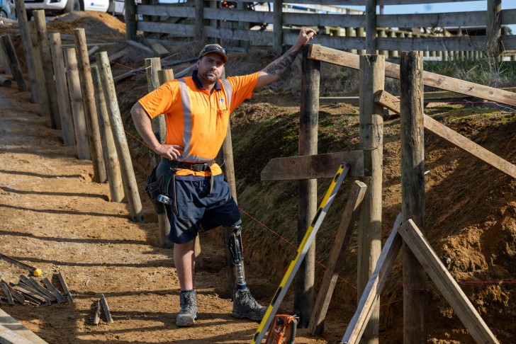 Cory McKinnon wearing his prosthetic leg standing on a construction site.