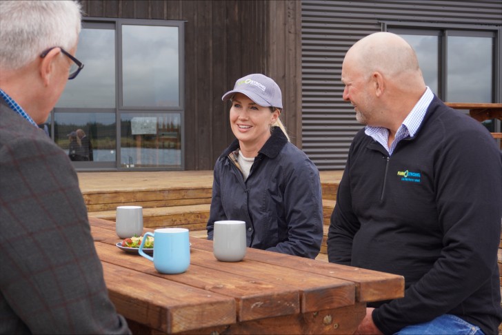 Hon Nicola Grigg sitting on an outdoor table having coffee with dairy farmer Geoff Spark.