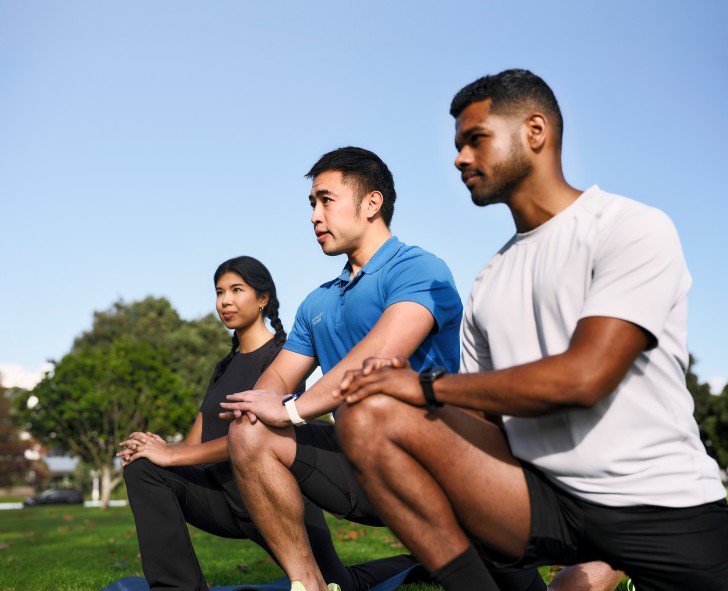 Two men and a woman kneeling down to do stretches on a sports field.
