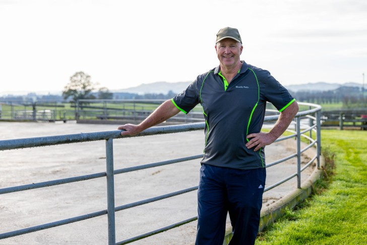John Moorby leaning on a fence on his farm and smiling.