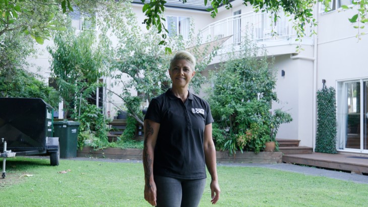 Rongoā Māori practitioner Jolie Davis standing in her garden and smiling at the camera. 