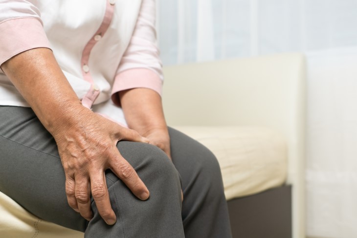 An older person sitting down holding their knee in pain.