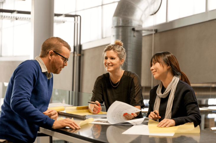 A man and two women having a meeting while standing at an office desk.
