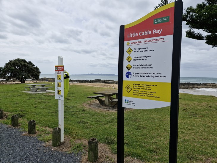 A sign highlighting the water hazards at a beach with a rescue device mounted on a post nearby. 