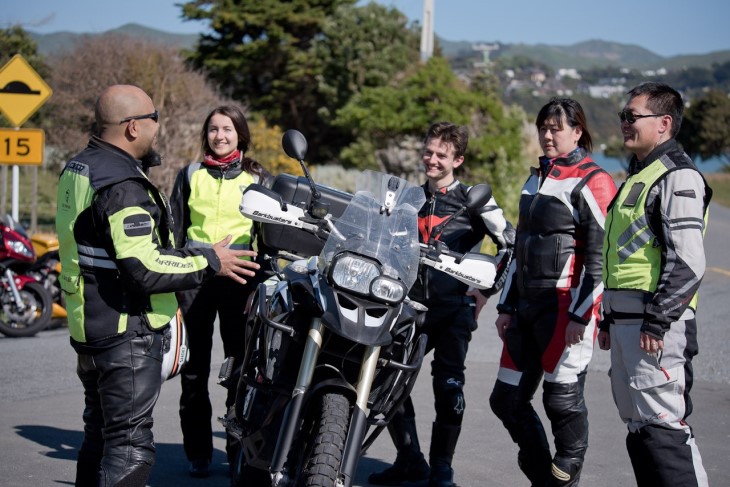 A group of riders standing around a motorbike and talking.