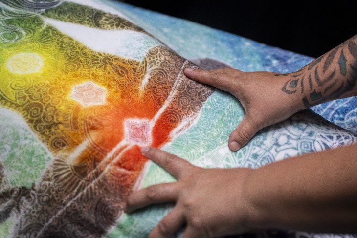A close-up shot of a rongoā Māori practitioner placing her hands on the back of a woman.