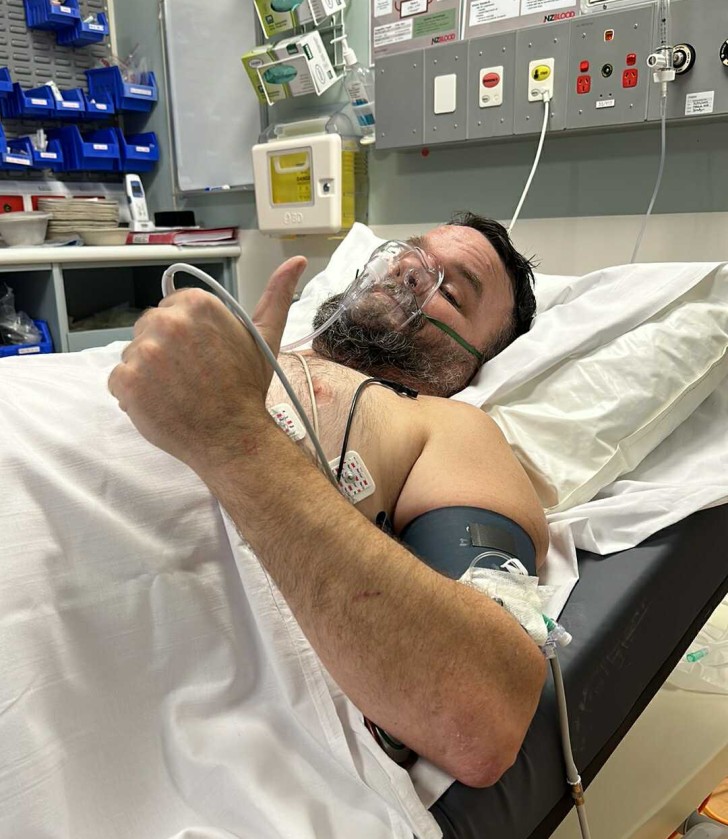 Steve Davies lying in a hospital bed giving the thumbs up. 