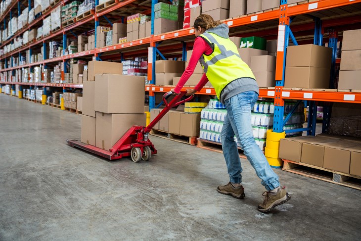 A female worker pushing a trolley with boxes across a factory floor.