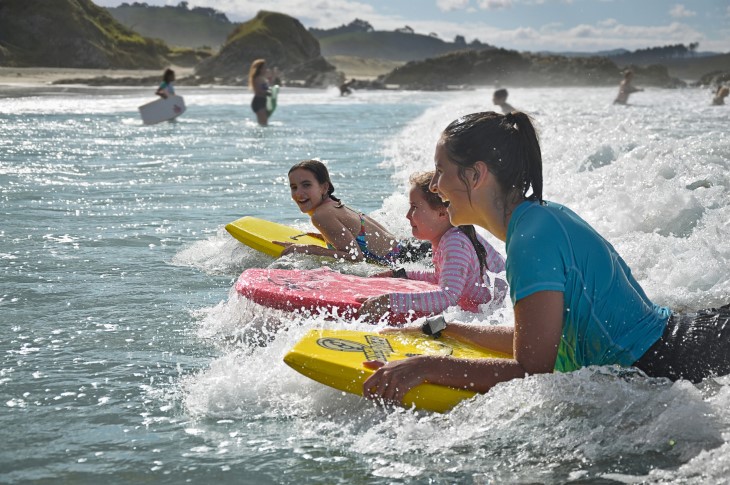 A woman and two girls lying on boogie boards to surf a wave.