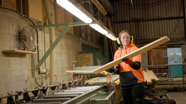 A woman holding a piece of timber next to a machine at Westco Lumber.